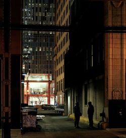 Silhouette people walking on illuminated street amidst buildings at night