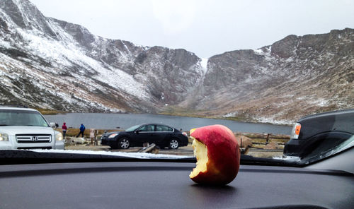Close-up of eaten apple on dashboard against lake by mountains during winter