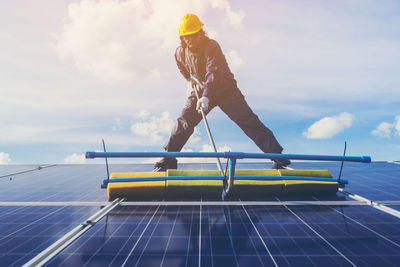 Low angle view of male technician cleaning solar panels against sky