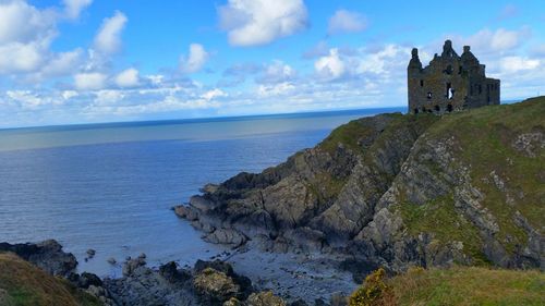 Dunskey castle on cliff by sea against sky