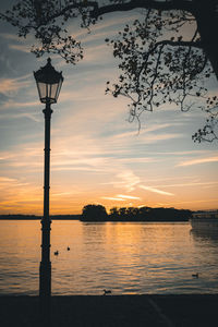 Silhouette street by lake against sky during sunset