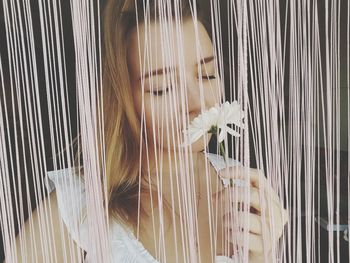 Close-up of woman smelling flower amidst thread