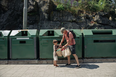 Grandfather and grandson holding garbage bags in front of bins
