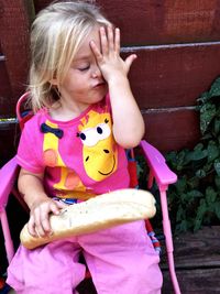 Irritated cute girl holding bread while sitting on chair in yard