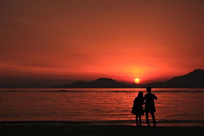 Silhouette couple standing at beach against orange sky