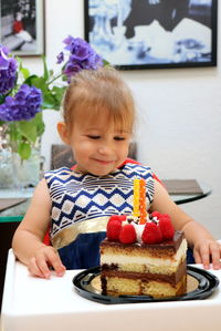 Portrait of cute smiling little girl with birthday cake with two candles 