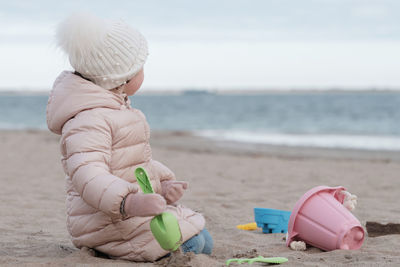 Little girl is digging in the sand on a cold day at the beach