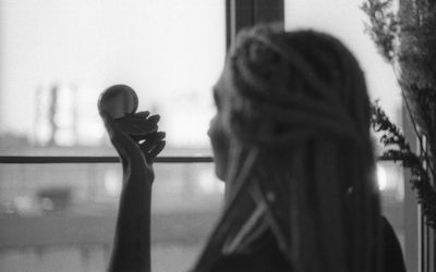 Side view of woman looking herself in mirror by window