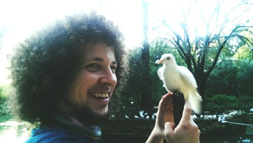 Close-up portrait of young man holding camera against sky