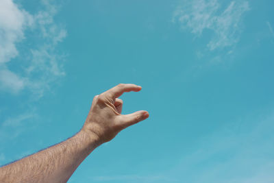 Cropped hand gesturing against sky