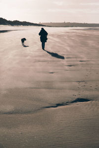 Full length of person walking with dog at beach against sky