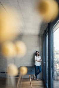 Smiling woman standing with arms crossed by glass window at home