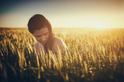 Woman sitting amidst plants on field against sky during sunset