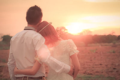 Rear view of couple standing on field at sunset