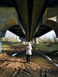 Rear view of woman standing under bridge