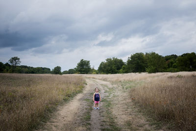Baby girl standing on field against cloudy sky