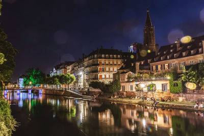 Illuminated buildings by river against sky at night