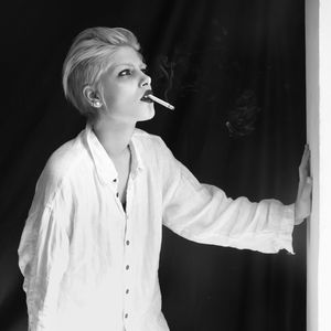 Mid adult woman smoking cigarette looking away while standing against black background
