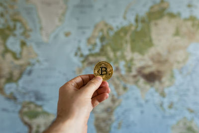 Close-up of hand holding bit coin against world map