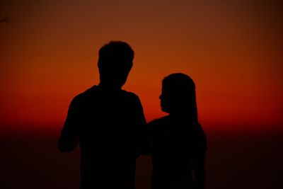 Silhouette couple standing against orange sky during sunset