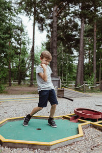 Full length of cheerful boy playing miniature golf in backyard during vacation