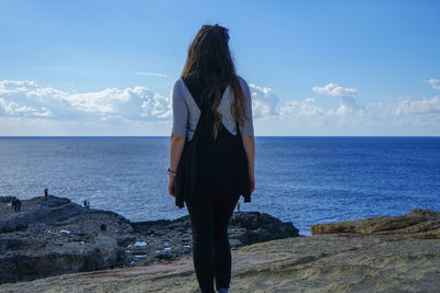 Rear view of woman standing by sea against sky