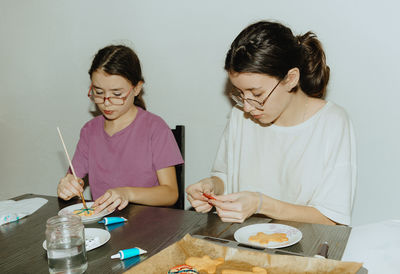 Two girls color cookies while sitting at the table.