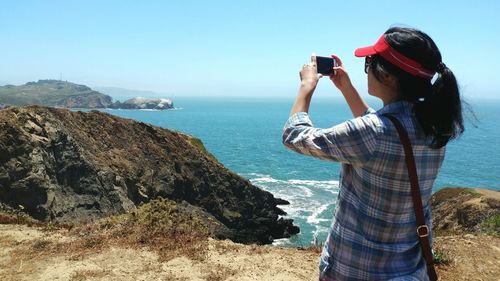 Woman photographing sea through smart phone while standing on cliff