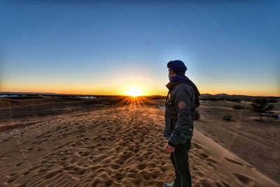 Man standing on sand at beach against clear sky during sunset