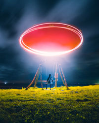 Rear view of person sitting on swing on land by sea at night