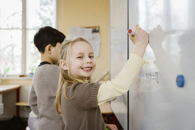 Portrait of smiling blond girl writing on whiteboard in classroom