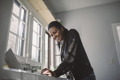 Smiling female professional looking at laptop while standing at home office