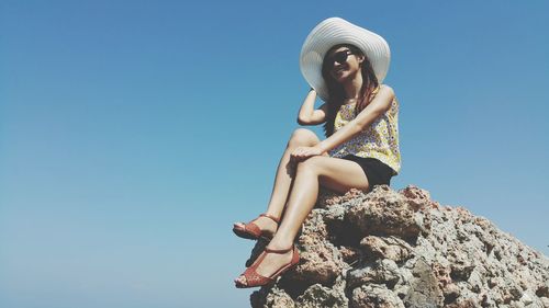 Woman sitting on rock against clear blue sky