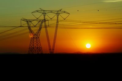 Silhouette electricity pylon on field against orange sky