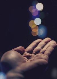 Cropped image of hand against illuminated lights at night