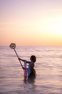 Young woman holding wand in sea during sunset