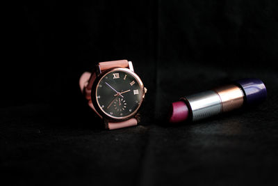 Close-up of wristwatch and lipstick against black background