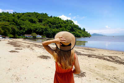 Young woman with hat relaxing enjoying looking view of beach ocean on hot summer day in brazil.