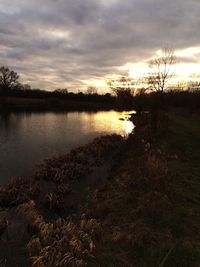 Scenic view of lake against cloudy sky at sunset