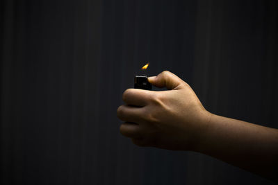 Close-up of hand holding cigarette against black background