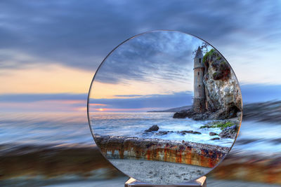 Close-up of glass of sea against sunset sky