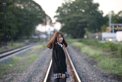 Portrait of smiling young woman standing on railroad track