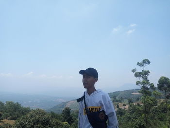 Young man standing by tree against sky