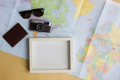 Map with photo frame, camera and sunglasses over the brown background.