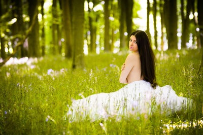 Young woman sitting on grass against trees