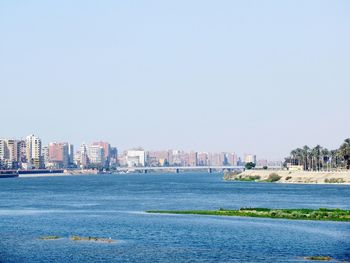 Sea by buildings in city against clear sky