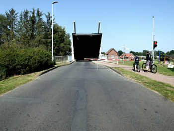 Empty road by plants in city against clear sky