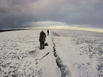 People walking on snow covered landscape against sky