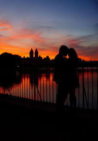 Silhouette couple standing by railing against sky during sunset