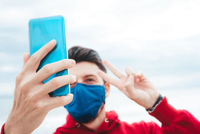 Close-up of man wearing mask taking selfie while standing against sky